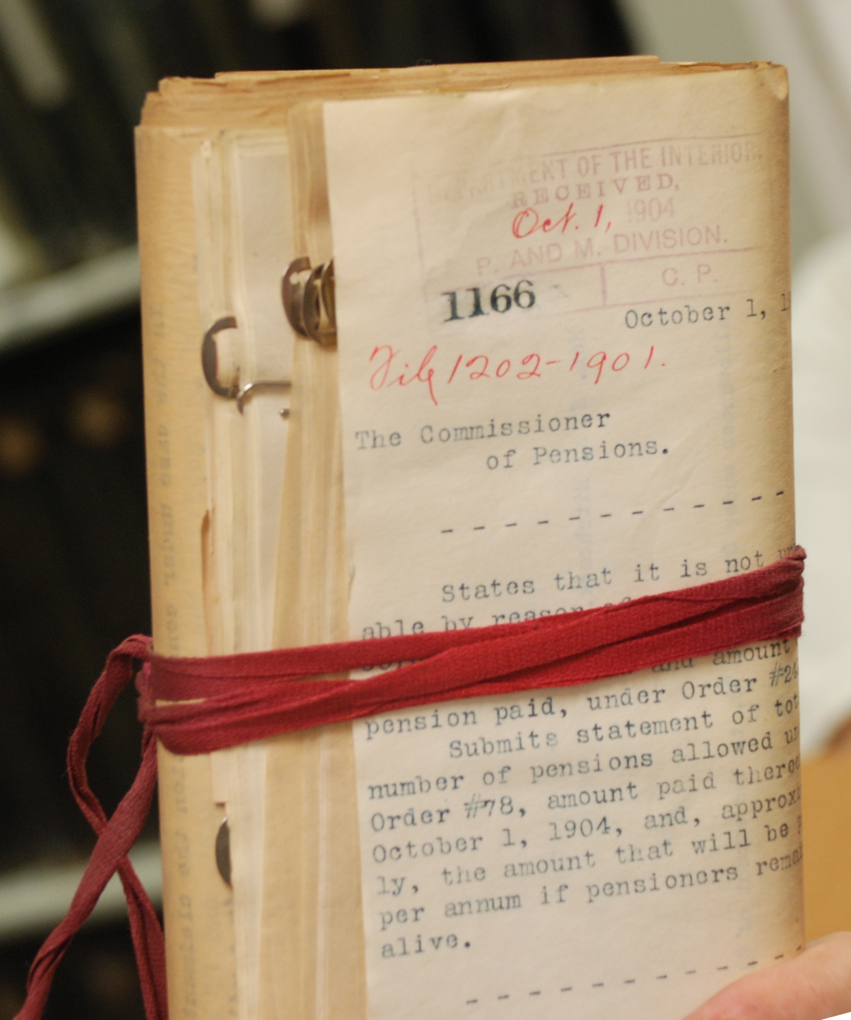 Bundle of US pension documents from 1906 bound in red tape. Jarek Tuszyński / CC-BY-SA-3.0 & GDFL via https://commons.wikimedia.org/wiki/File:NARA_Backstage_Pass_(2011-08)_-_14.jpg